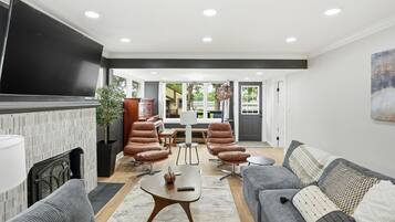 A modern living room with a fireplace, leather chairs, a grey sofa, and a flat-screen TV.
