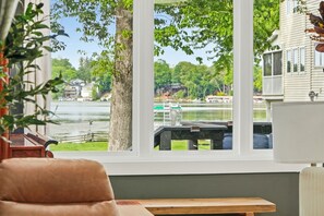 Una habitación con un ventanal grande que da a un lago, una mesa de madera y una silla.