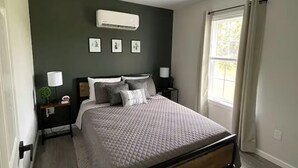 Una camera da letto con un letto, comodini, un condizionatore d'aria a parete e una finestra con tende.