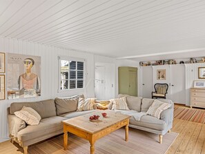 A living room with a beige sofa, a wooden coffee table, and a window with shutters.