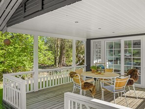 A covered outdoor patio with a wooden deck, white railings, and a round table with chairs.