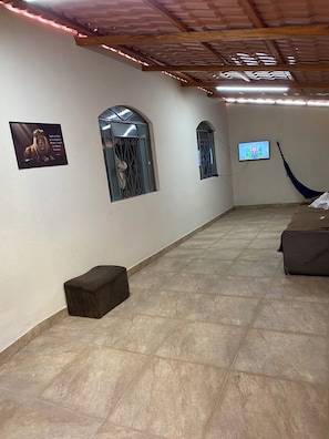 Una habitación amplia con piso de baldosas, una hamaca, un televisor y ventanas decorativas.