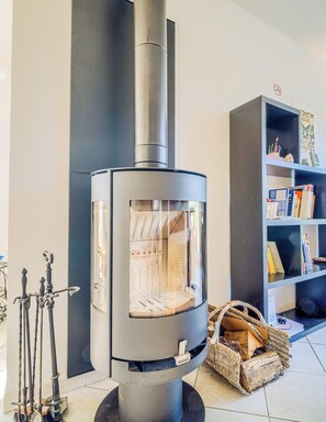 Ein moderner Kaminofen mit Glasscheibe, ein schwarzes Bücherregal und ein gewebter Korb mit Brennholz.