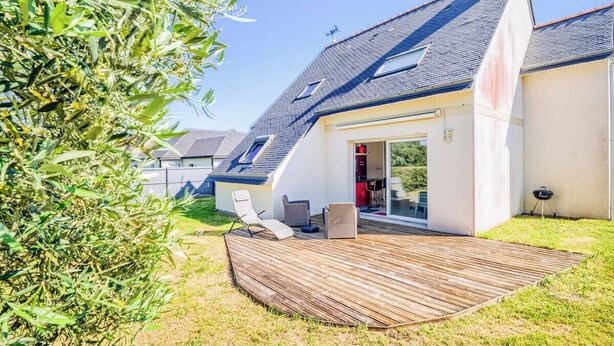 Een modern huis met een schuin dak, een houten terras en een glazen deur naar de binnenruimte.