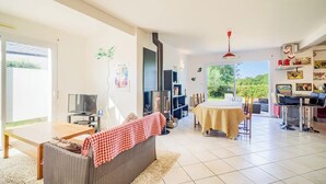 Een woonkamer met een bank, een tafel, een televisie, een open haard en uitzicht op groen.