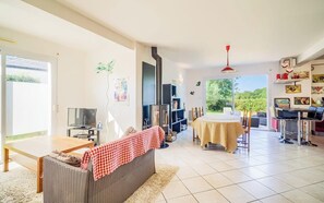Ein Wohnzimmer mit einer Couch, einem Tisch, einem Fernseher, einem Kamin und Blick auf Grünfläche.