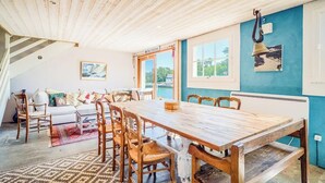 Un espace repas comprenant une table et des chaises en bois, un canapé et une vue sur l’extérieur.