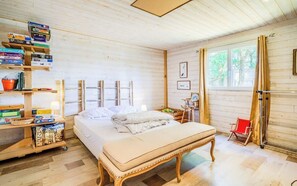 Ein Zimmer mit Holzboden, einem Bett, einem Nachttisch, einem Bücherregal und einem Fenster.