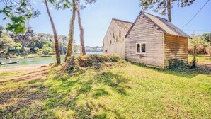 Une cabane en bois avec un toit à deux versants, entourée d’arbres et bordée par un plan d’eau.