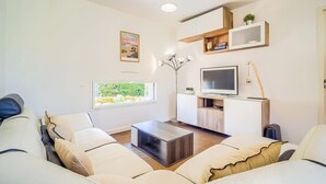 Moderni olohuone, jossa on sohva, sohvapöytä, televisio ja hyllyt.
