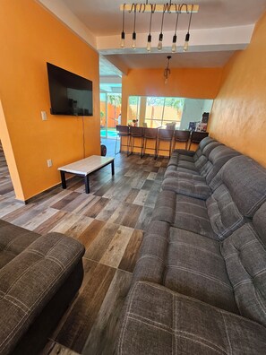 A living room with a sofa, a TV, a table, and a bar area with chairs. - Family Weekend: Private Pool, Barbeque, Sun and Relaxation (Xochitepec)