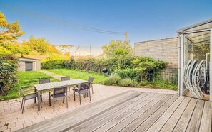 Eine Terrasse mit Tisch und Stühlen, ein Holzdeck und ein Gartenbereich mit Grill.