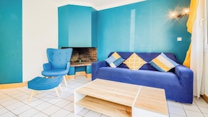 Une pièce avec un canapé bleu, un fauteuil bleu, une table basse et une cheminée.