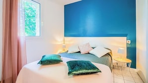 Une chambre avec un grand lit, une table de chevet, une lampe et une vue sur la verdure.