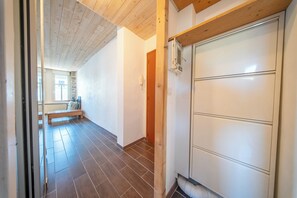 A hallway with a wooden ceiling, a white door, and a bench in the background. - Pause Vacances : Grand T3 Lumineux (Guidel)
