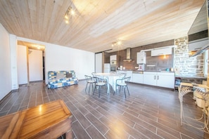 A spacious kitchen with a dining area, wooden ceiling, and a stone accent wall. - Pause Vacances : Grand T3 Lumineux (Guidel)