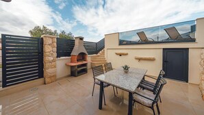 Eine Außenpatio mit Steinmauer, einem Ziegelofen, einem Tisch mit Stühlen und einem Glasgeländer mit Blick auf die Umgebung.