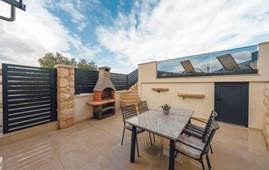 Eine Außenpatio mit Steinmauer, einem Ziegelofen, einem Tisch mit Stühlen und einem Glasgeländer mit Blick auf die Umgebung.