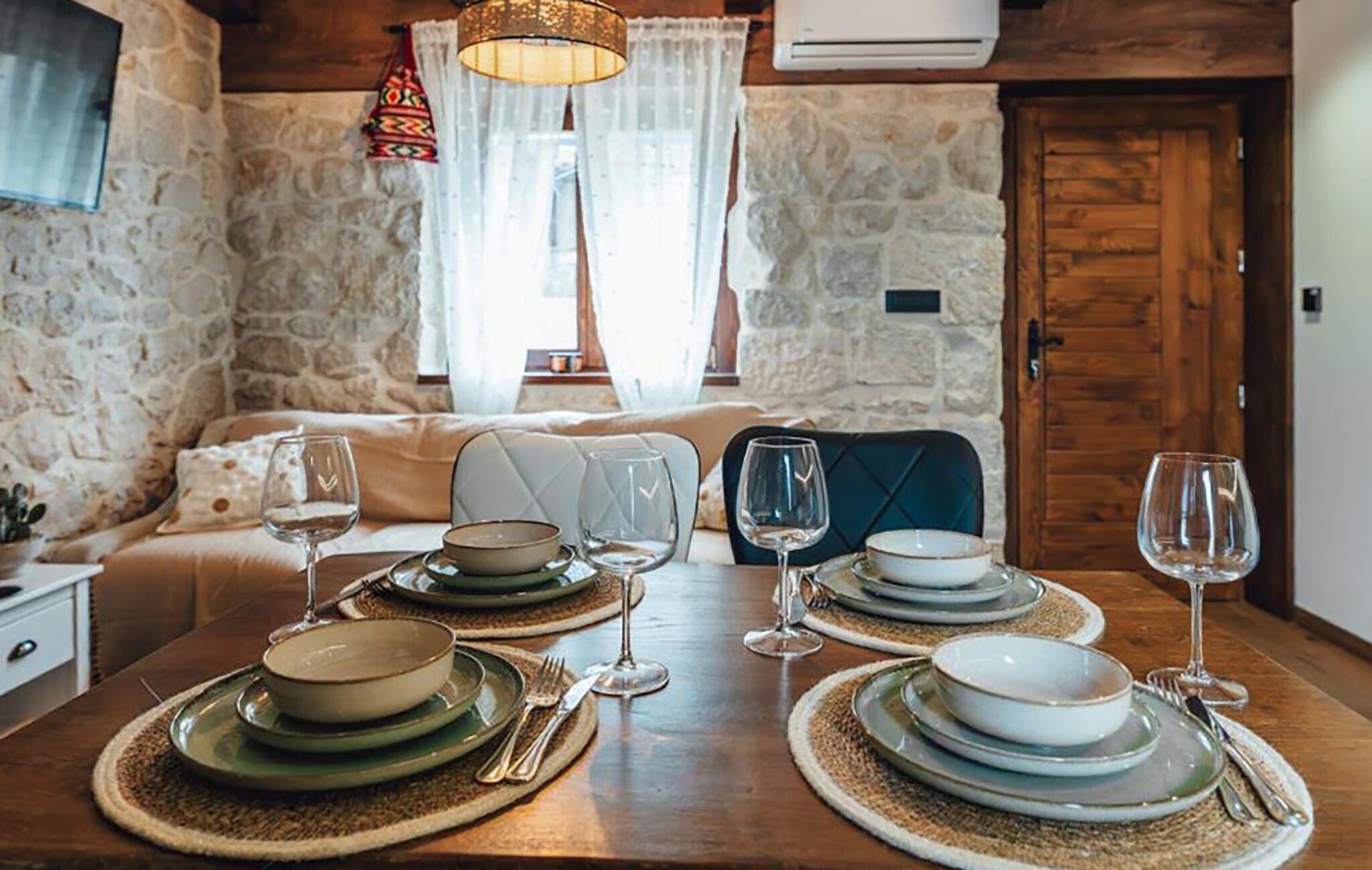 Une table à manger dressée avec des assiettes, des bols et des verres à vin, entourée de murs en pierre et de meubles en bois.