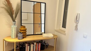 Een hoekje met een houten console, een spiegel, een vaas met pampa gras en een telefoon aan de muur.
