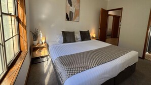 Une chambre à coucher avec un grand lit, une table de chevet avec une lampe, une fenêtre et un ventilateur de plafond.