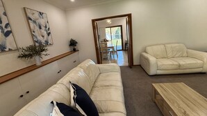 Un salon avec un canapé beige, une table basse en bois et un coin repas visible à travers une porte ouverte.