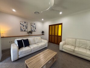 A living room with two white leather sofas, a wooden coffee table, and a wall-mounted shelf with decorative items.