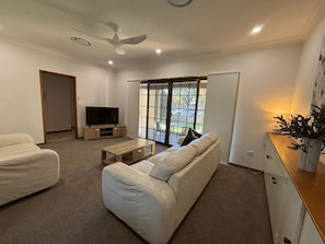 A living room with a sofa, a coffee table, a TV, a ceiling fan, and a sliding glass door leading to a balcony.