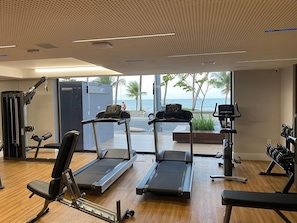 Ein Fitnessstudio mit Laufbändern, Krafttrainingsgeräten und Blick auf den Ozean.