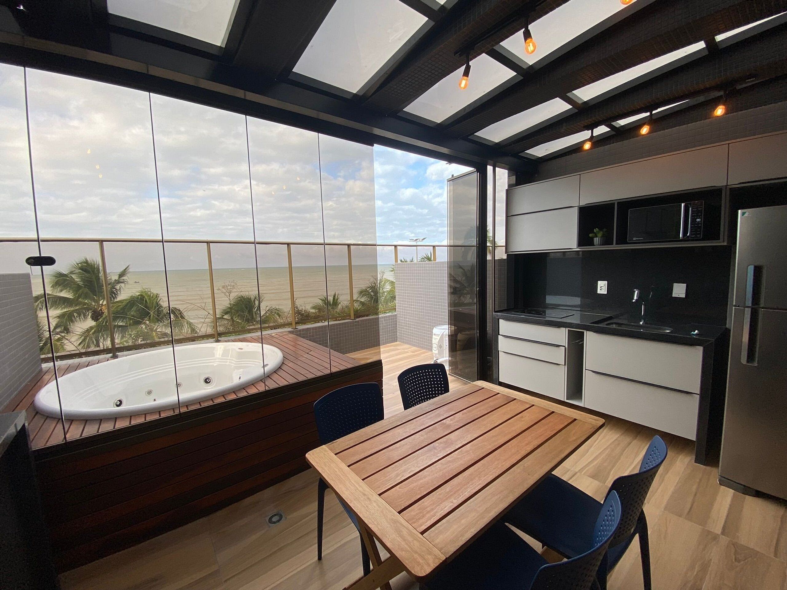 A modern kitchen with a view of the beach, a wooden table, and a hot tub.