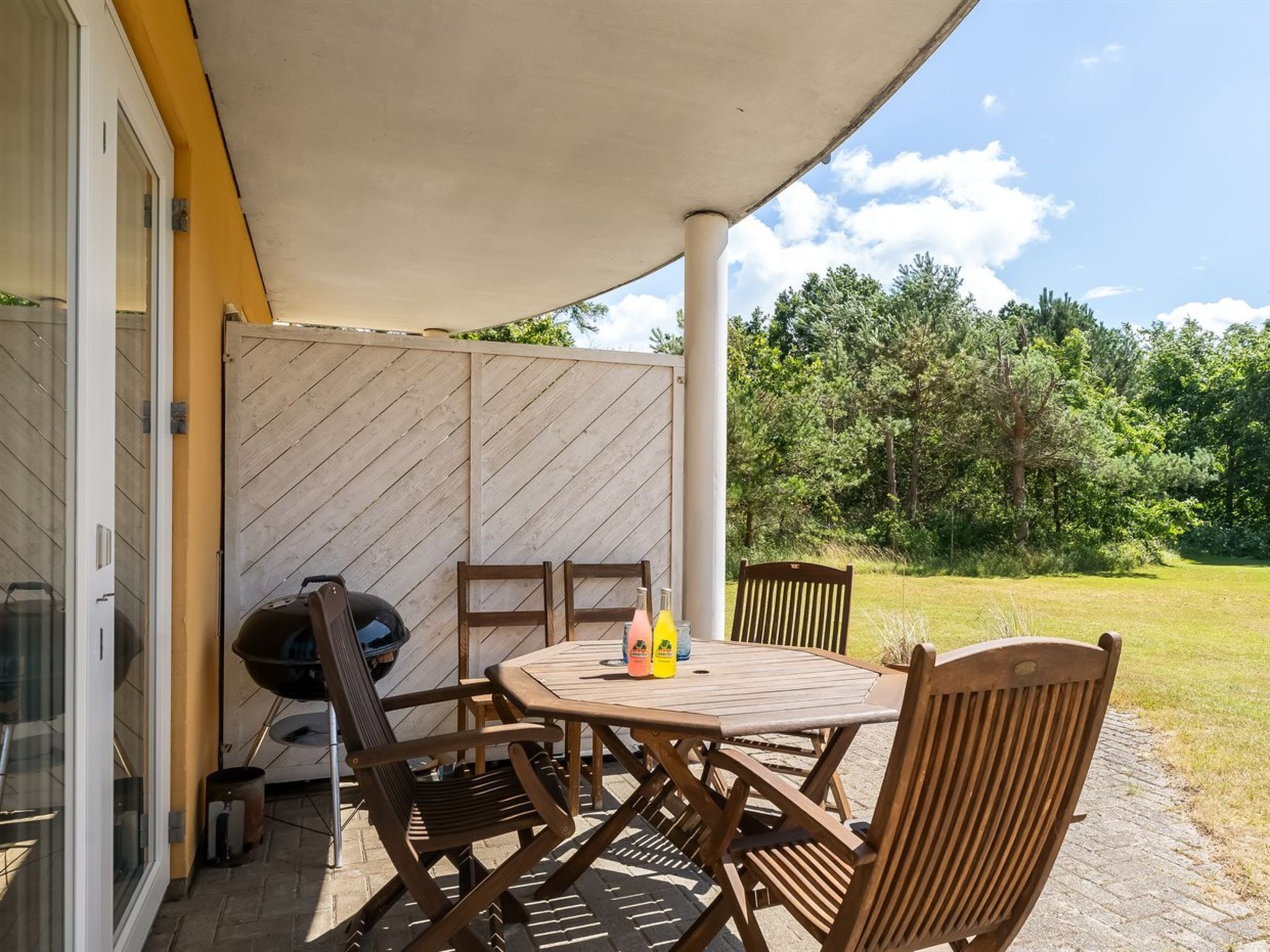 A covered patio with a table and chairs, a grill, and a glass door leading to an outdoor area.