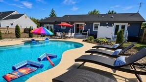 A swimming pool with lounge chairs and a deck, surrounded by a house and a fence. - Lefty’s Poolside Retreat (Lewes)