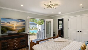 A bedroom with a bed, a TV, a wooden dresser, and a view of a swimming pool. - Lefty’s Poolside Retreat (Lewes)