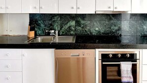 Una cocina con armarios blancos, encimera negra, lavavajillas de acero inoxidable y horno con una toalla colgada del pomo.
