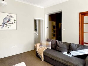 Una sala de estar con un sofá gris, un cuadro enmarcado de pájaros, una puerta y una estantería.