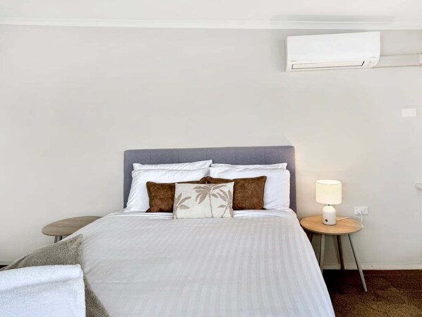 Une chambre d’hôtel avec un lit, une table de chevet avec une lampe et un appareil de climatisation fixé au mur.