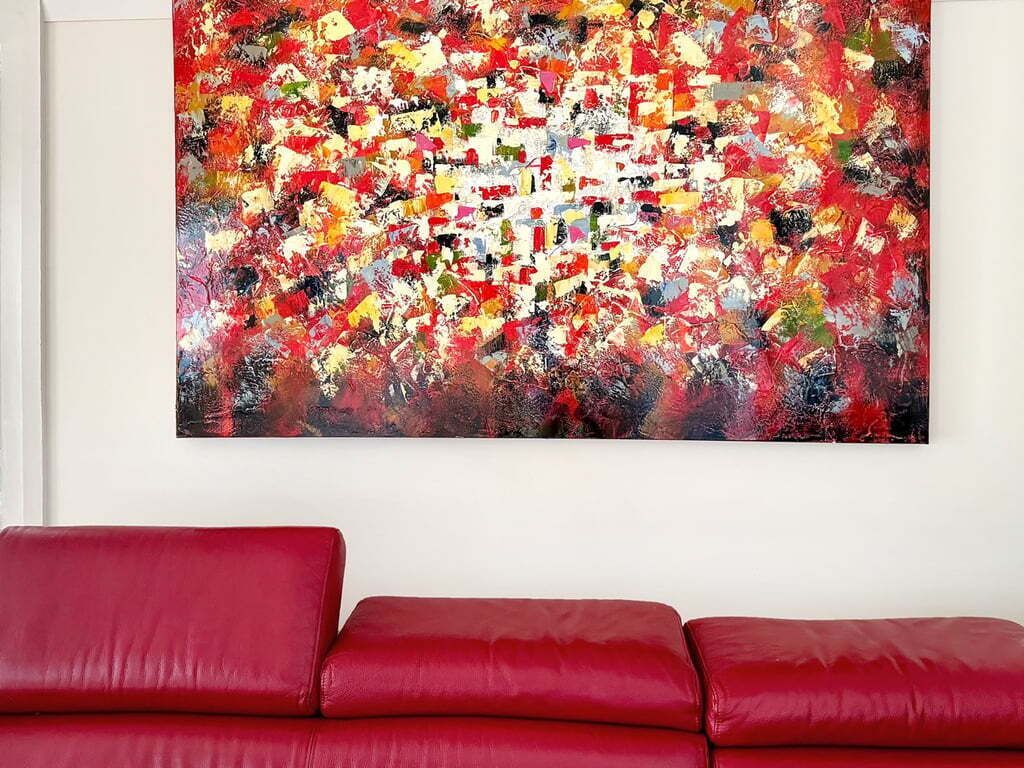 A red sofa in a room with a colorful abstract painting on the wall.