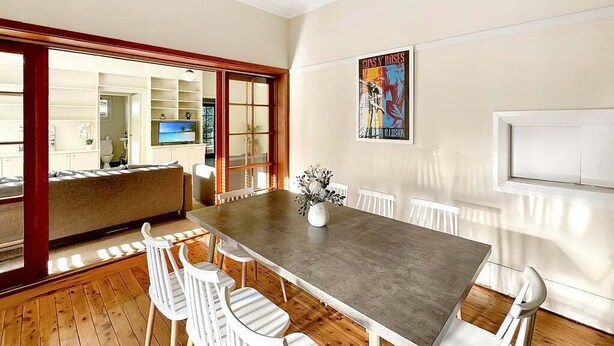 Un comedor con una mesa larga, sillas blancas y un jarrón de flores.