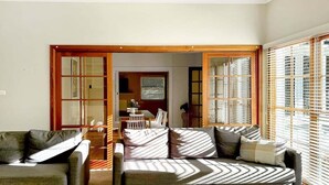 A living room with a sofa, a chair, and a dining table. There is a sliding door leading to another room. - Gurwood Stay - All of the Comforts (Wagga Wagga)