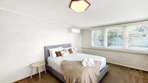 Un dormitorio con cama, mesita de noche, ventana con persianas e iluminación en el techo.