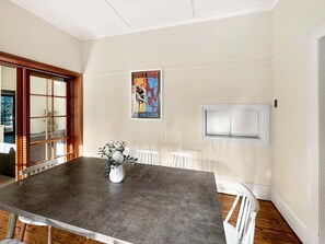 Un coin repas avec une table en béton, des chaises blanches, un vase avec des fleurs, une affiche au mur et une porte blanche.