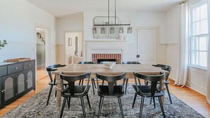 Uma área de jantar espaçosa com uma grande mesa de madeira, cadeiras pretas e um lustre moderno.