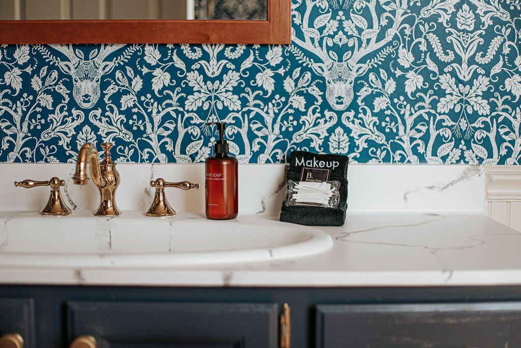 A bathroom with a white sink, gold faucets, and a red soap bottle. There is a black sign with the word "Makeup" on it.