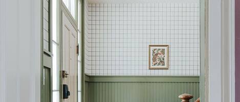 Un couloir doté d’un plancher en bois, de lambris verts, d’une colonne décorative en bois et d’un tableau encadré accroché au mur.