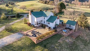 Uma casa grande e branca com telhado verde, um pátio com mobiliário exterior e uma piscina.