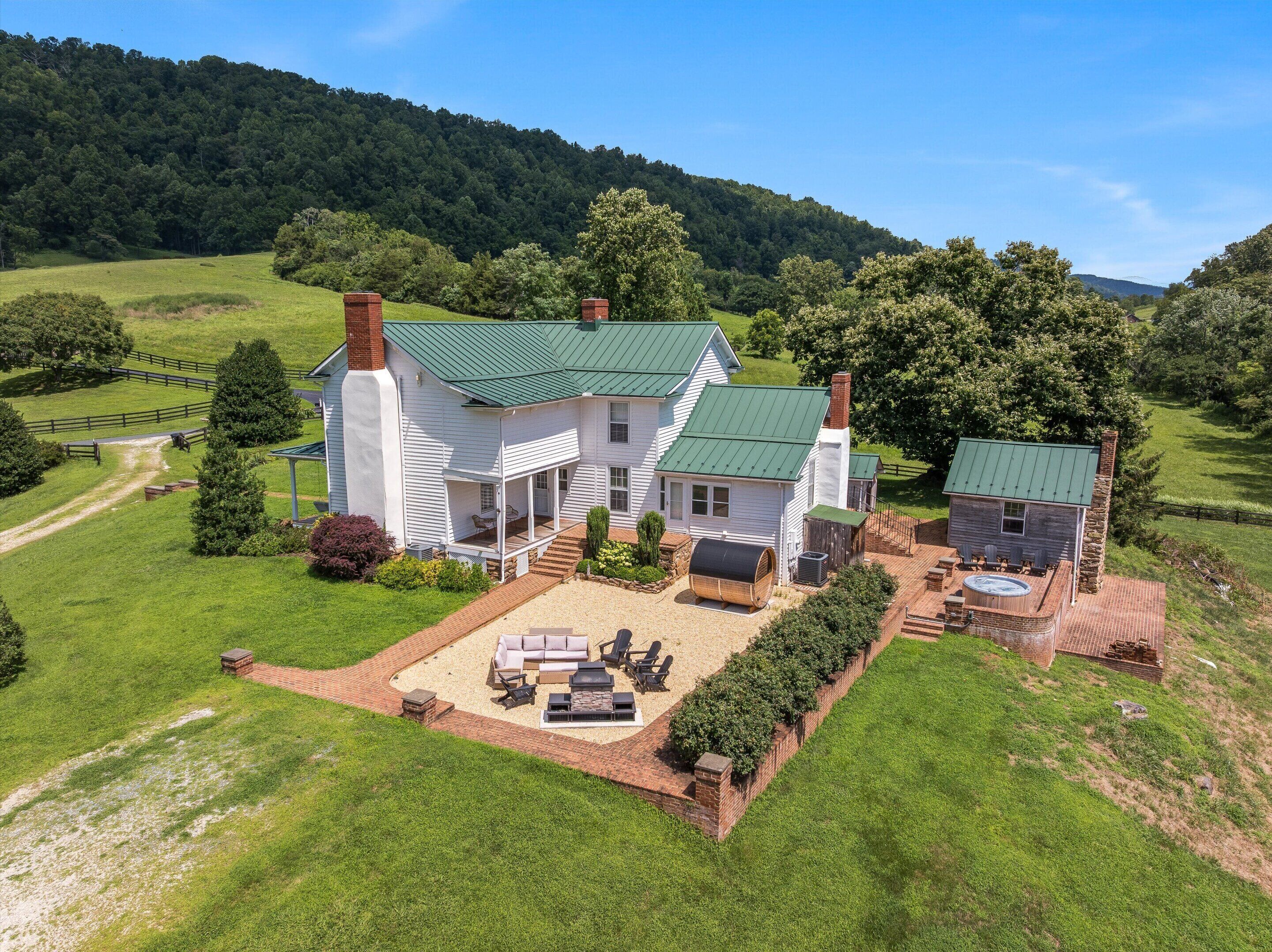 A large white house with a green roof, a patio with outdoor furniture, and a stone fireplace.