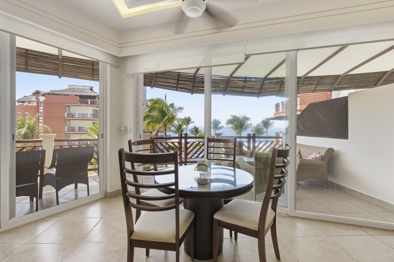 A room with a round table and chairs, large windows, and a ceiling fan.