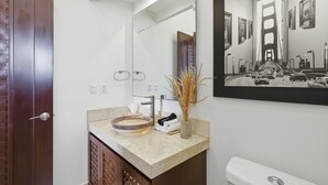 Een badkamer met een houten deur, een beige aanrecht, een grote spiegel en een foto van een stadsgezicht in een lijst.