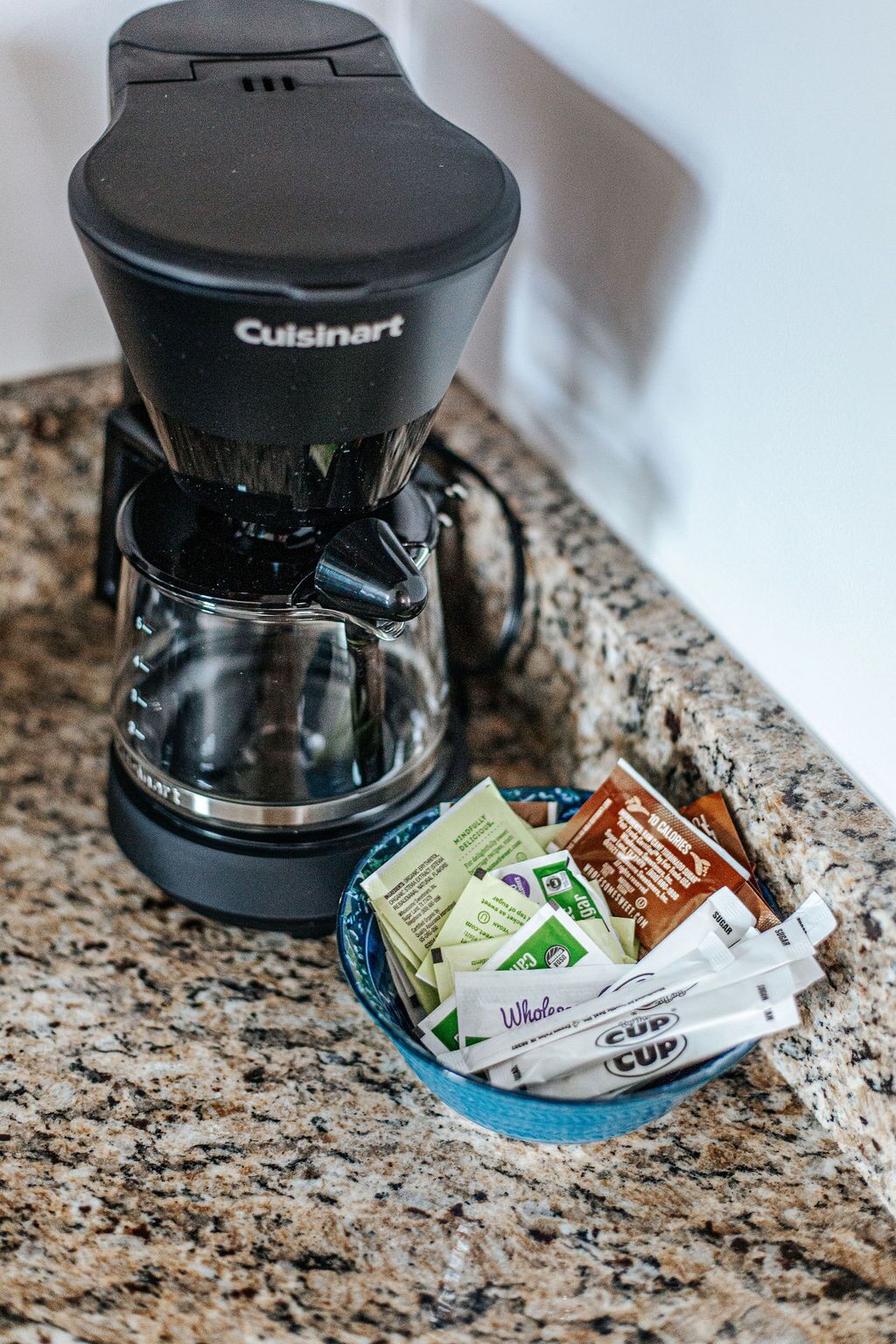A Cuisinart coffee maker on a granite countertop with a blue bowl containing coffee pods.