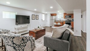 A modern living room with a flat-screen TV, patterned sofas, a coffee table, and a kitchen in the background. - Cavalier Cocoon (Charlottesville)